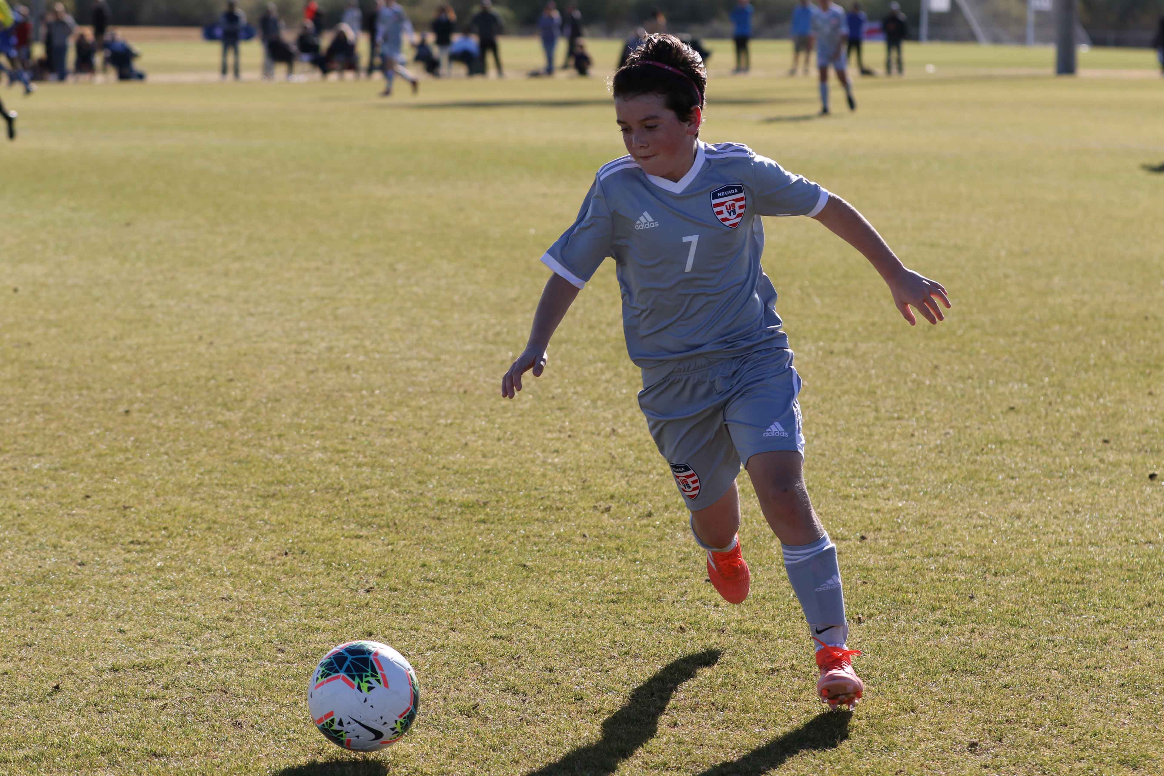 kid dribling the ball in the middle of the soccer field
