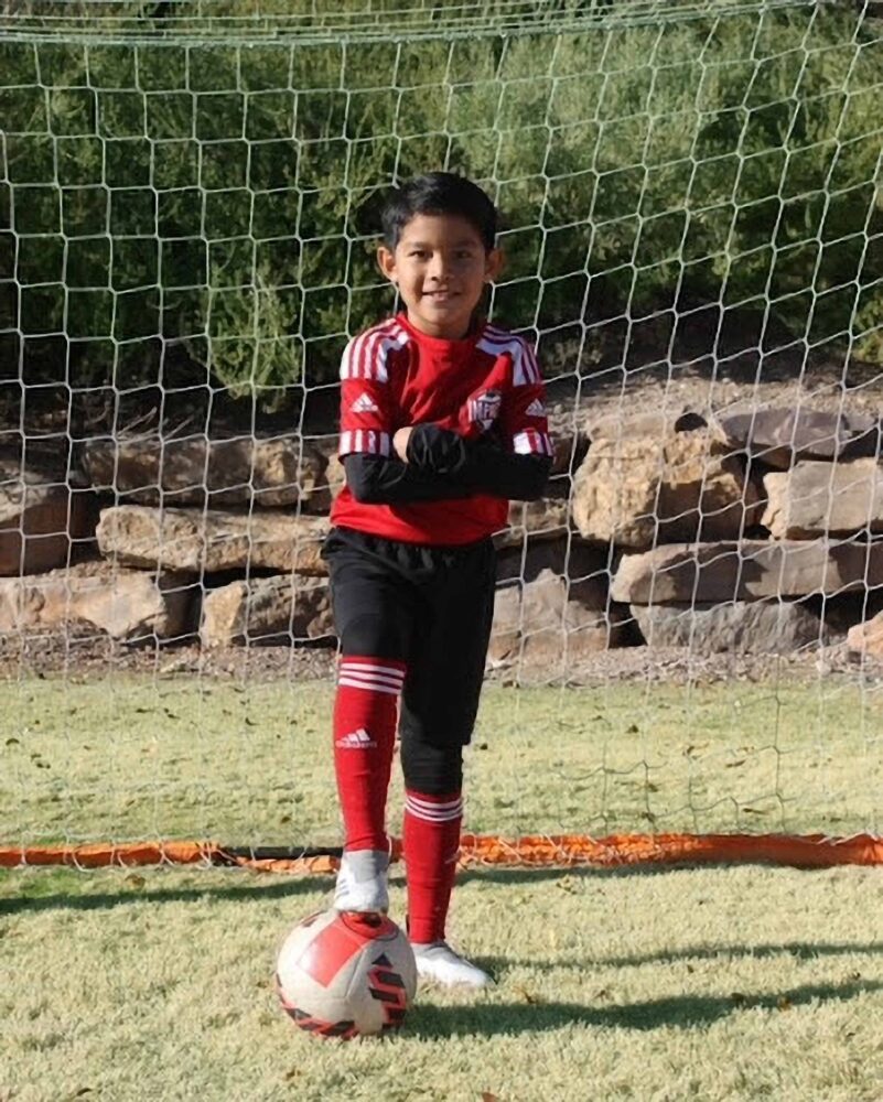 kid stainding on the ground with a soccer ball under his foot