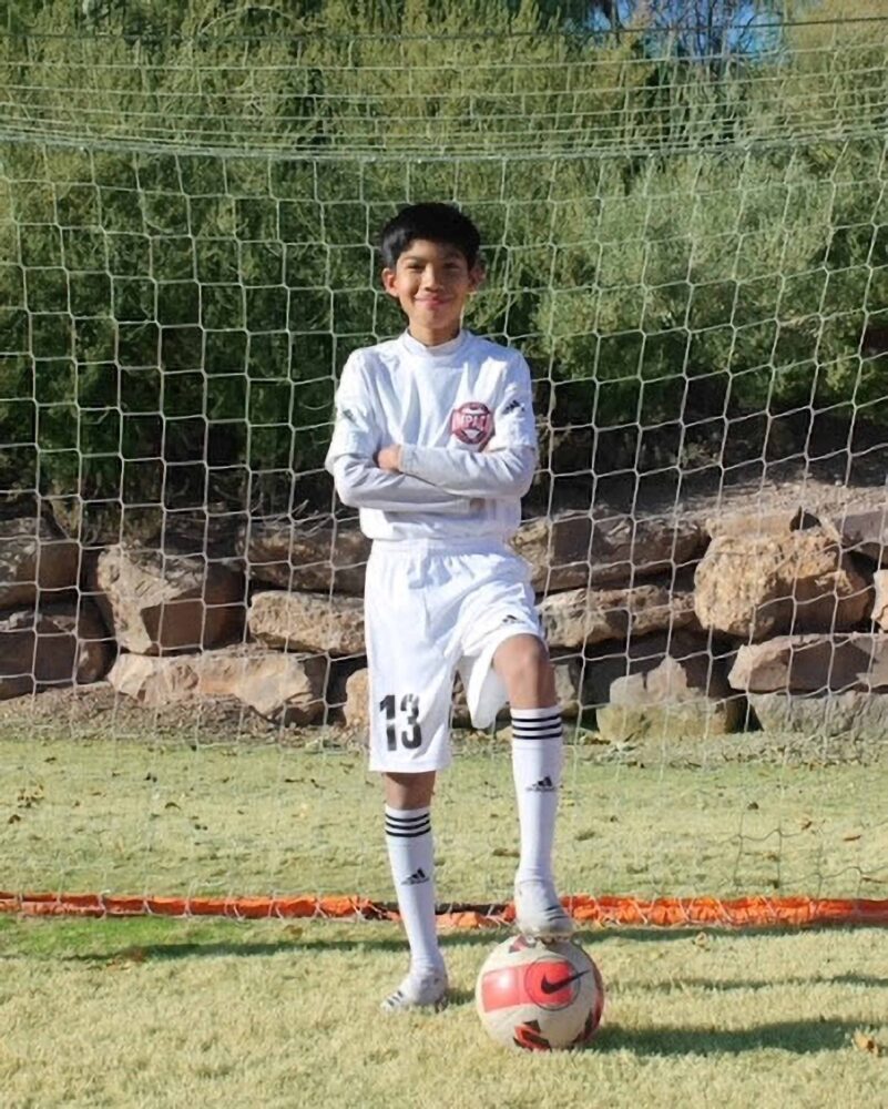 kid in white uniform posing with a ball under his left foot